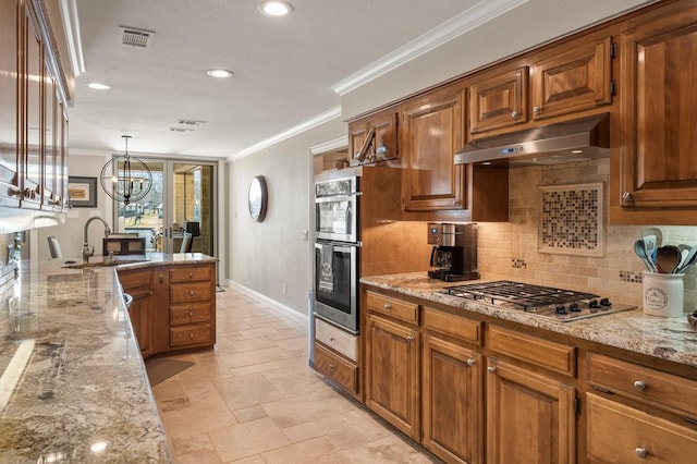 kitchen with crown molding, under cabinet range hood, brown cabinets, appliances with stainless steel finishes, and a sink