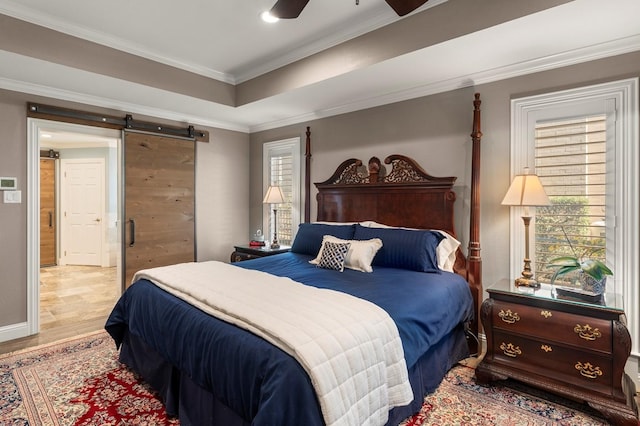 bedroom with baseboards, ornamental molding, light wood-style floors, a barn door, and a raised ceiling