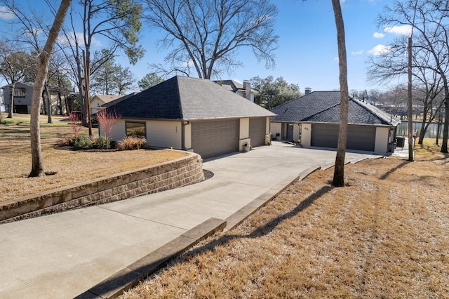 view of side of home with an attached garage, a chimney, driveway, and a shingled roof