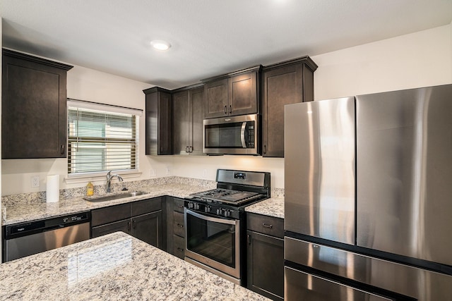 kitchen with dark brown cabinetry, light stone countertops, appliances with stainless steel finishes, and a sink