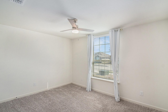 spare room featuring light carpet, visible vents, a ceiling fan, and baseboards