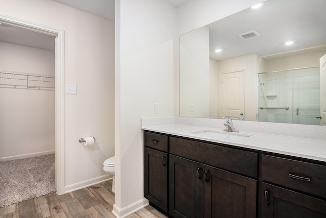 bathroom with a walk in closet, toilet, wood finished floors, a shower stall, and baseboards