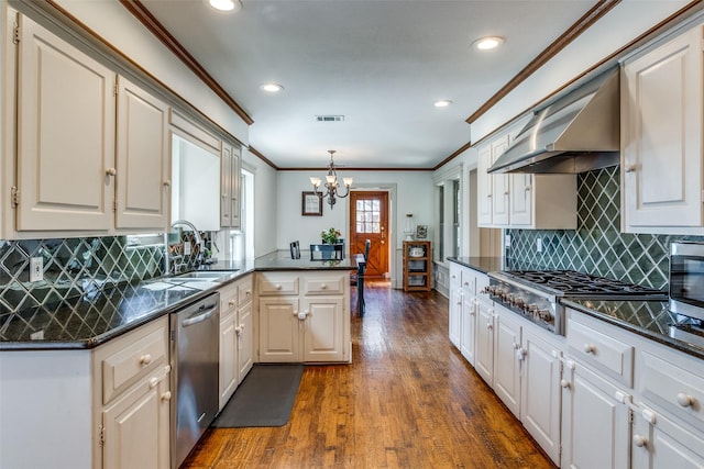 kitchen featuring visible vents, a peninsula, a sink, stainless steel appliances, and exhaust hood