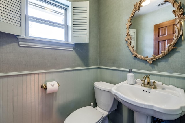 bathroom with a sink, toilet, visible vents, and wainscoting