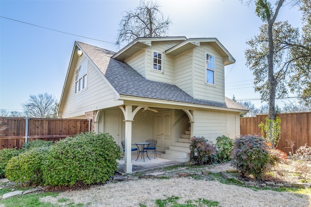 view of front facade featuring a shingled roof, a patio, and fence