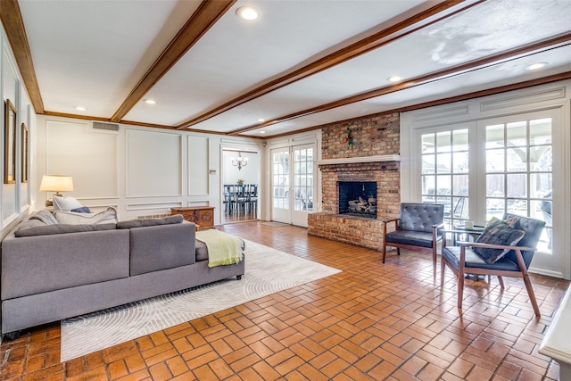 living room with brick floor, a brick fireplace, french doors, beamed ceiling, and a decorative wall