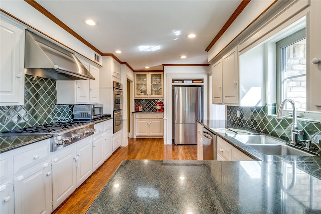 kitchen with a sink, wood finished floors, range hood, appliances with stainless steel finishes, and crown molding