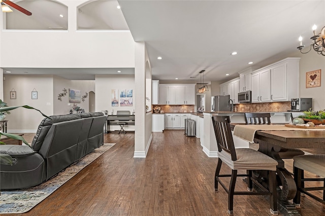 dining area with ceiling fan with notable chandelier, dark wood finished floors, recessed lighting, arched walkways, and baseboards