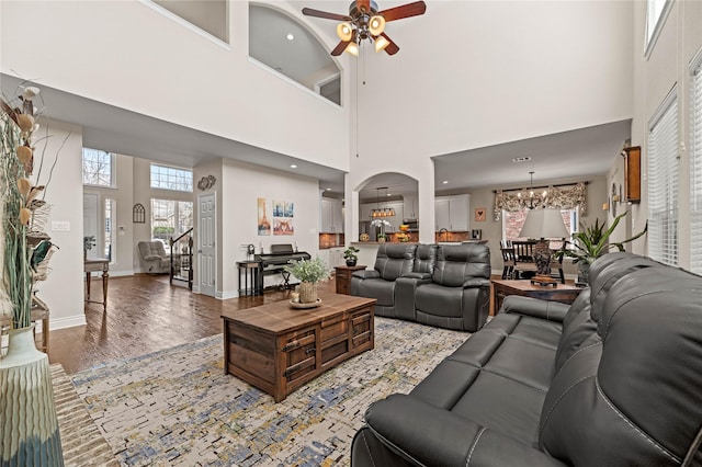 living room with ceiling fan with notable chandelier, a high ceiling, light wood-type flooring, and baseboards