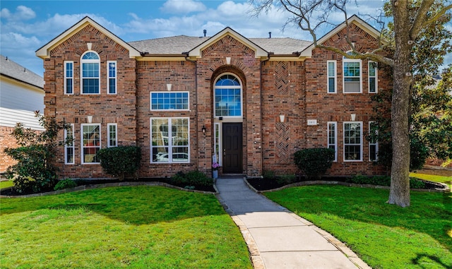 traditional-style house featuring a front lawn, brick siding, and a shingled roof