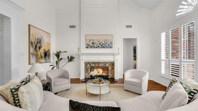 living area with visible vents, baseboards, wood finished floors, a glass covered fireplace, and high vaulted ceiling