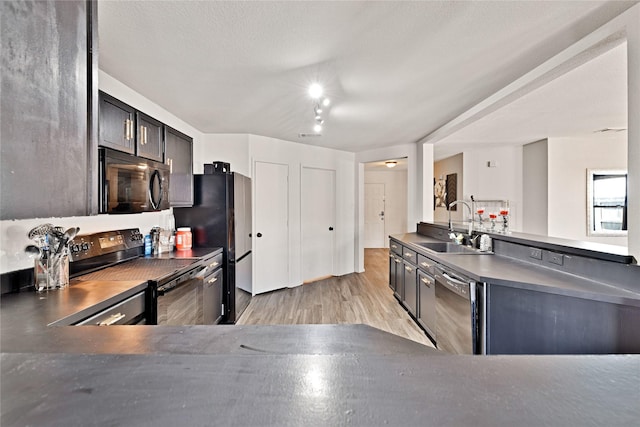 kitchen featuring dark countertops, light wood-style flooring, a peninsula, black appliances, and a sink