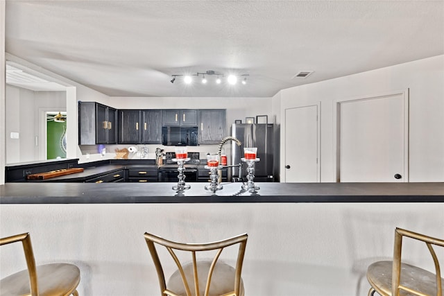 kitchen featuring dark countertops, range with electric cooktop, black microwave, a kitchen breakfast bar, and freestanding refrigerator