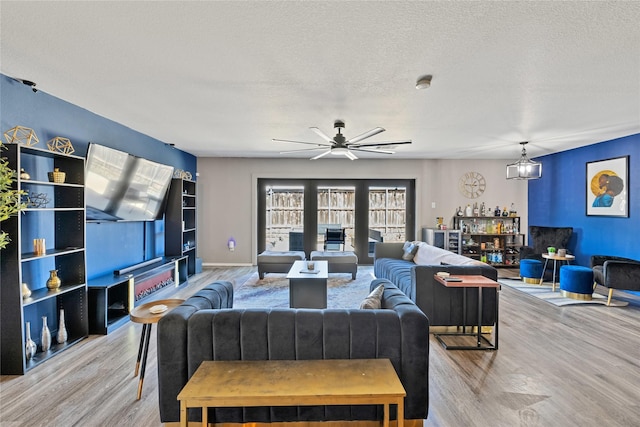 living area with ceiling fan, baseboards, a textured ceiling, and wood finished floors