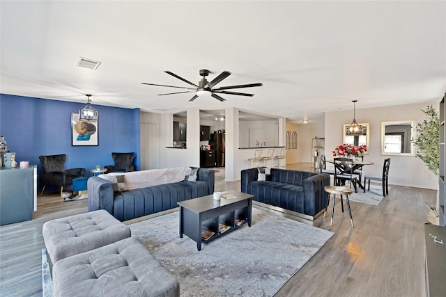 living area with ceiling fan with notable chandelier, visible vents, and light wood finished floors