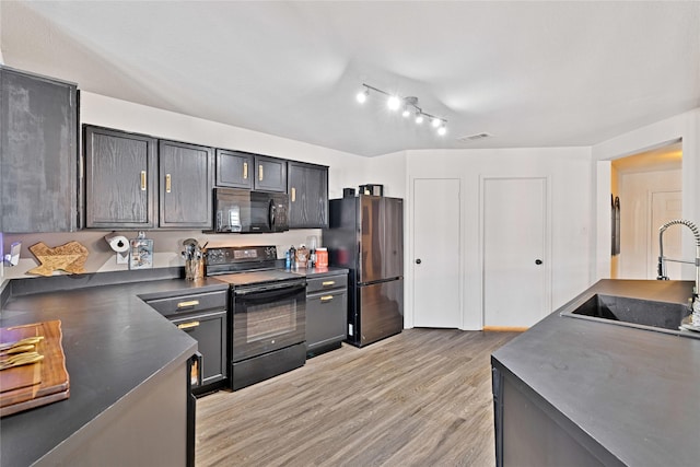 kitchen featuring visible vents, a sink, black appliances, light wood-style floors, and dark countertops