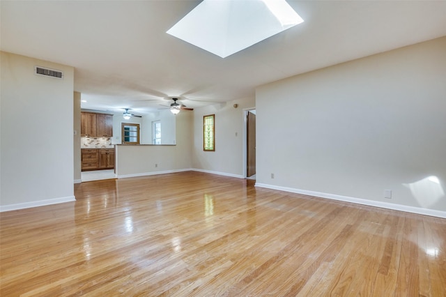 unfurnished living room with visible vents, a ceiling fan, a skylight, light wood finished floors, and baseboards