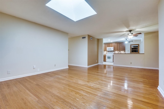 unfurnished living room featuring baseboards, light wood-style floors, a skylight, and a ceiling fan