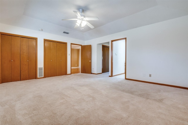 unfurnished bedroom featuring multiple closets, baseboards, visible vents, and light carpet