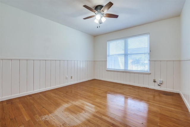 unfurnished room featuring wood-type flooring, ceiling fan, and wainscoting