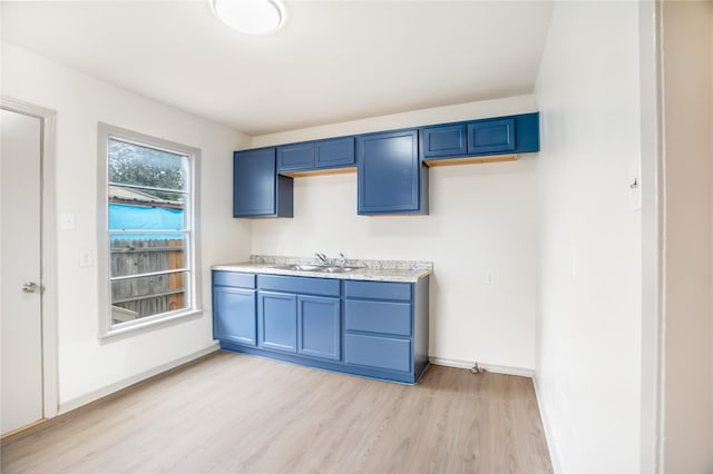 kitchen featuring a sink, blue cabinets, light wood-style flooring, and light countertops