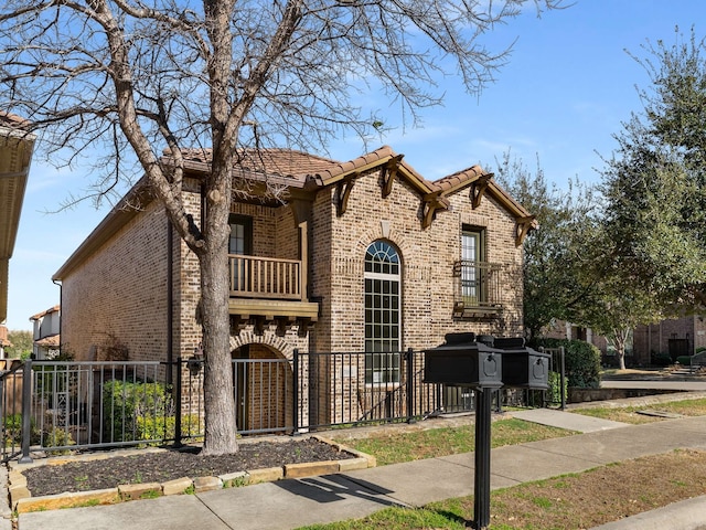 view of front of property with brick siding, a fenced front yard, a tiled roof, a balcony, and an attached garage