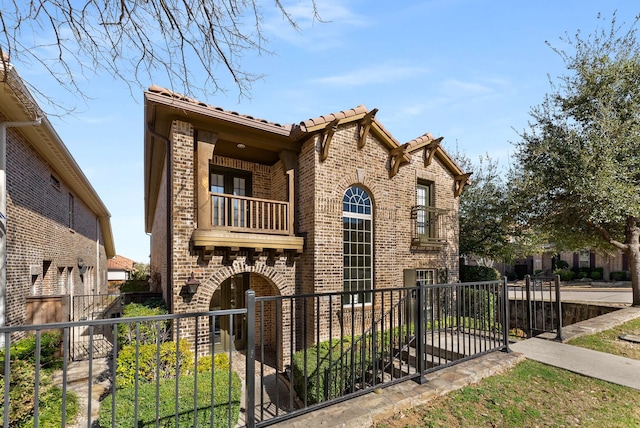 view of front of property with a fenced front yard, a tiled roof, brick siding, and a balcony