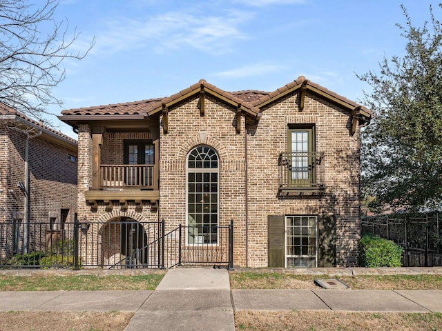 view of front of home with a tile roof, a balcony, brick siding, and a fenced front yard