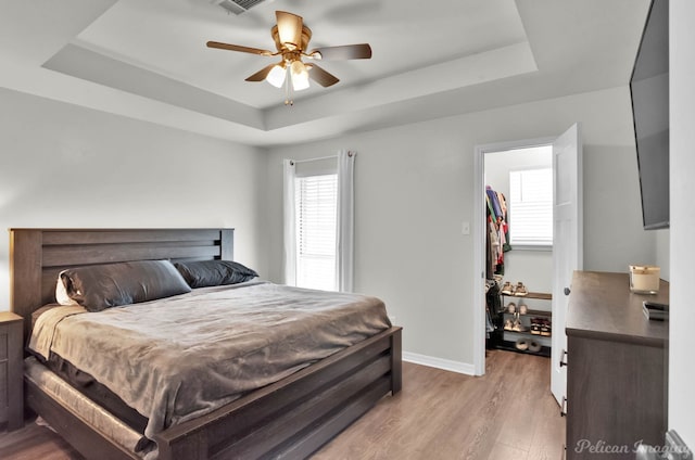 bedroom with light wood-type flooring, a tray ceiling, baseboards, and a walk in closet