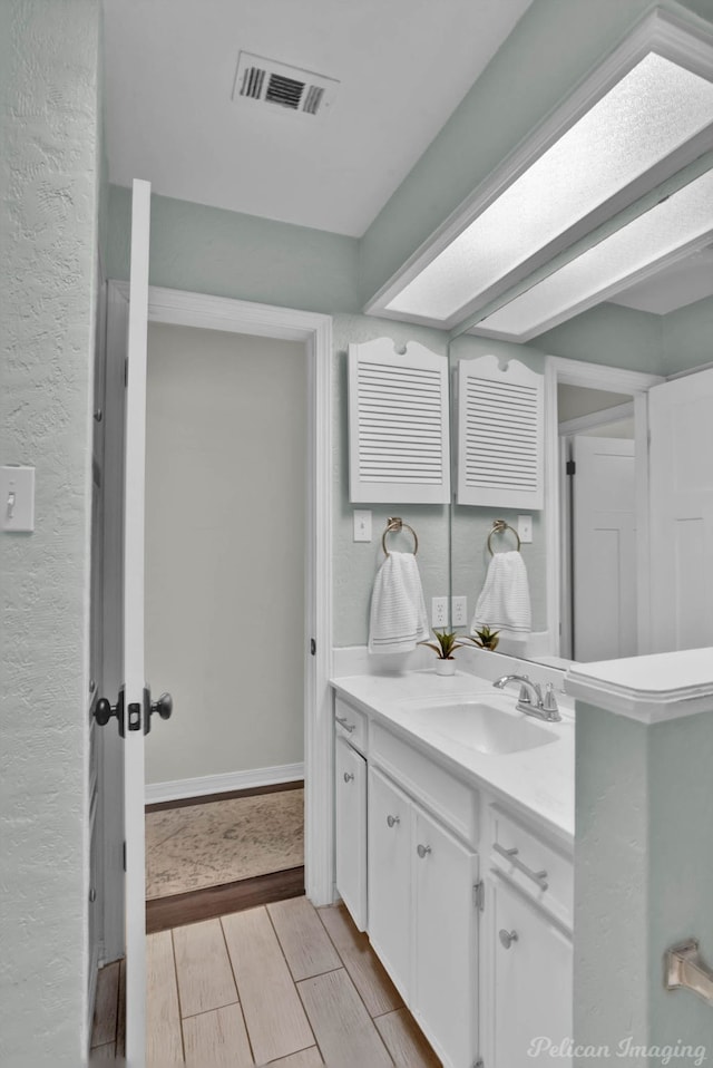 bathroom featuring wood finish floors, visible vents, baseboards, vanity, and a textured wall