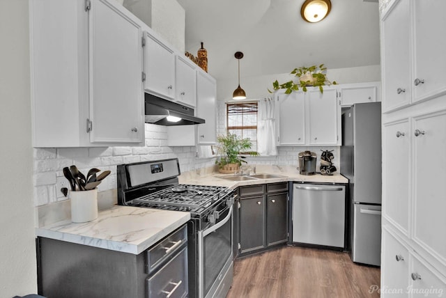 kitchen with a sink, stainless steel appliances, white cabinets, under cabinet range hood, and backsplash