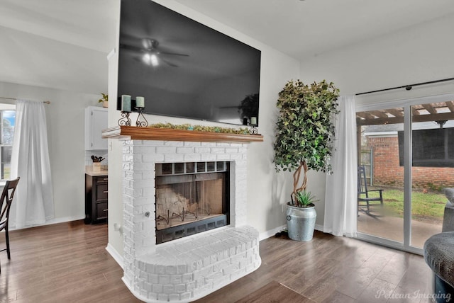 living room with a brick fireplace, baseboards, and wood finished floors