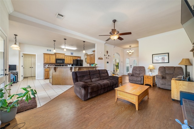 living area with arched walkways, visible vents, light wood-style floors, and ornamental molding