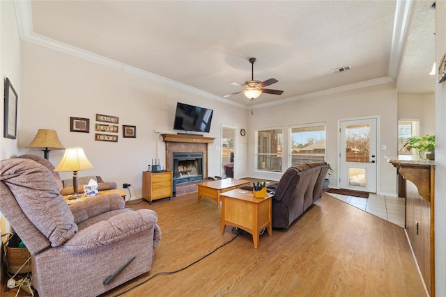 living area with visible vents, ornamental molding, light wood-style floors, a fireplace, and ceiling fan