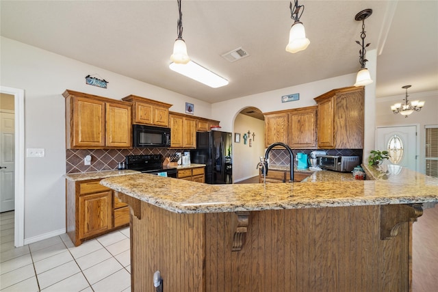 kitchen with visible vents, arched walkways, black appliances, a kitchen bar, and brown cabinets