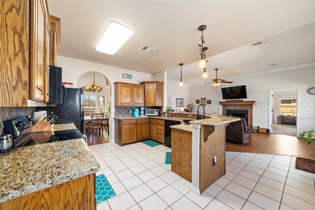 kitchen with black appliances, open floor plan, arched walkways, a peninsula, and a fireplace