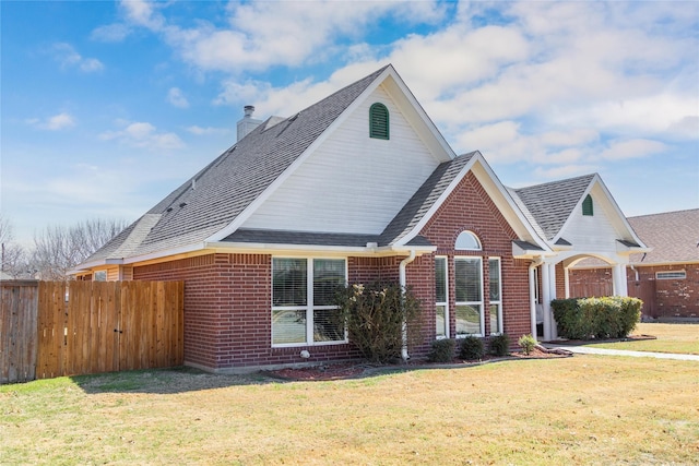 view of front of property featuring fence, roof with shingles, a front yard, brick siding, and a chimney