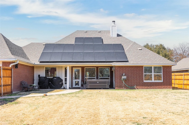 rear view of property featuring roof mounted solar panels, a lawn, brick siding, and a fenced backyard