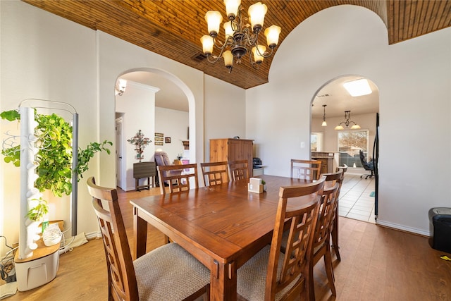 dining room with baseboards, lofted ceiling, arched walkways, hardwood / wood-style flooring, and a chandelier