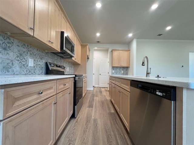 kitchen with light brown cabinetry, light stone counters, appliances with stainless steel finishes, wood finished floors, and a sink