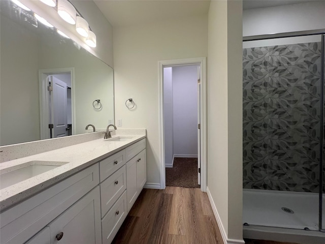 full bath featuring baseboards, double vanity, a stall shower, wood finished floors, and a sink