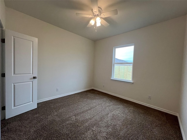 spare room with dark colored carpet, baseboards, and a ceiling fan