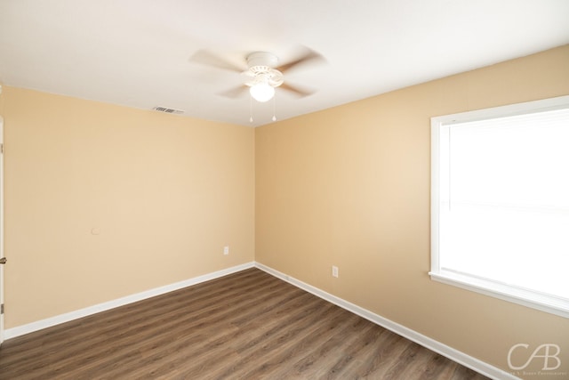 empty room featuring visible vents, a ceiling fan, dark wood-type flooring, and baseboards