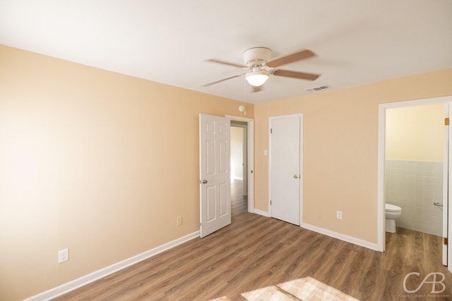 unfurnished bedroom featuring wood finished floors, visible vents, baseboards, ensuite bath, and tile walls