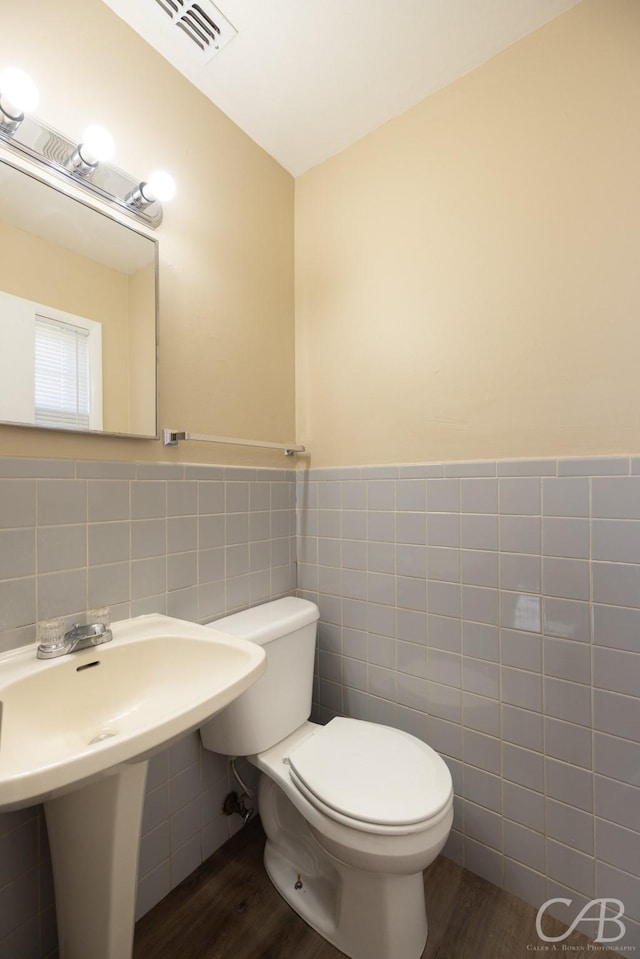 bathroom featuring visible vents, toilet, wood finished floors, tile walls, and wainscoting