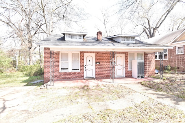 bungalow-style house with brick siding, a porch, and a chimney