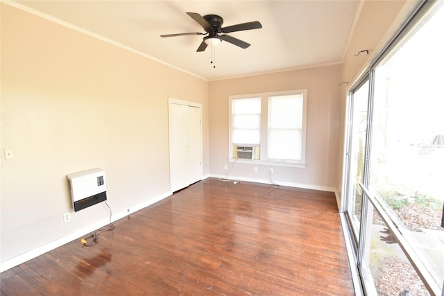 empty room featuring crown molding, baseboards, wood finished floors, heating unit, and a ceiling fan