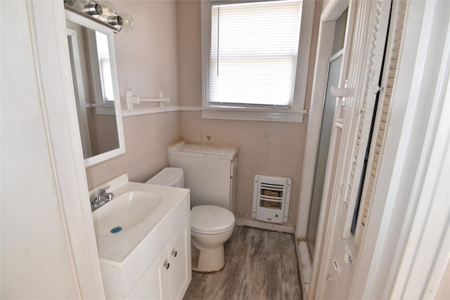 full bathroom featuring a wealth of natural light, heating unit, toilet, and wood finished floors