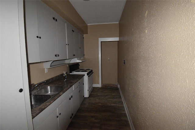 kitchen with dark countertops, white range with electric cooktop, a textured wall, white cabinets, and a sink