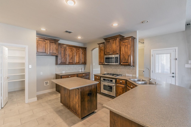 kitchen featuring stainless steel appliances, a sink, arched walkways, backsplash, and a kitchen island